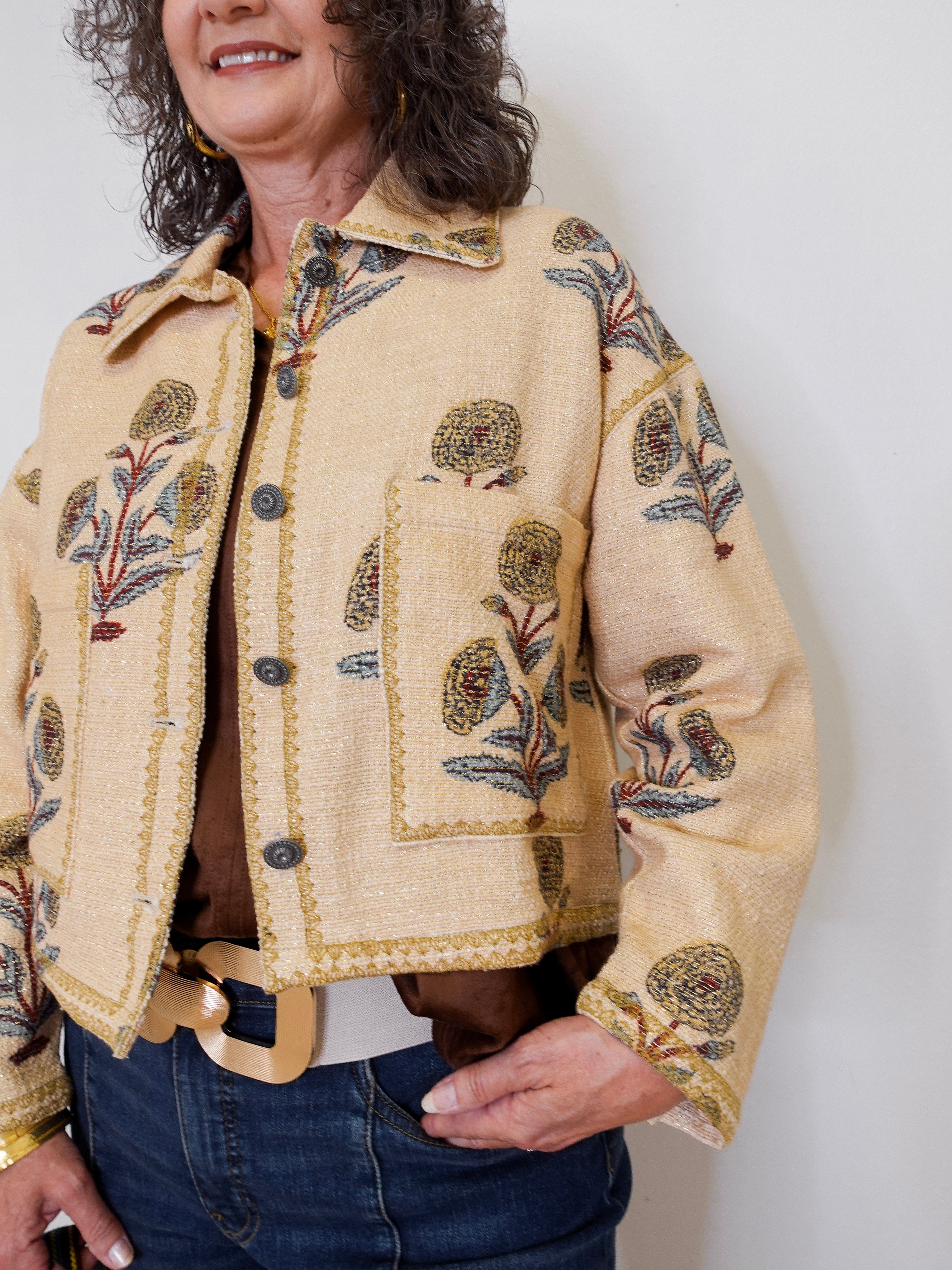 Woman wearing a beige embroidered jacket against a white background
