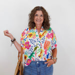 Woman wearing a colorful floral shirt with text, holding a straw bag against a white background