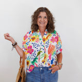 Woman wearing a colorful floral shirt with text, holding a straw bag against a white background