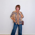 Woman wearing a patterned jacket and blue jeans against a white wall
