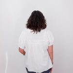 Person wearing a white blouse and blue jeans standing against a white wall.