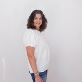 Woman wearing a white blouse and blue jeans against a plain background