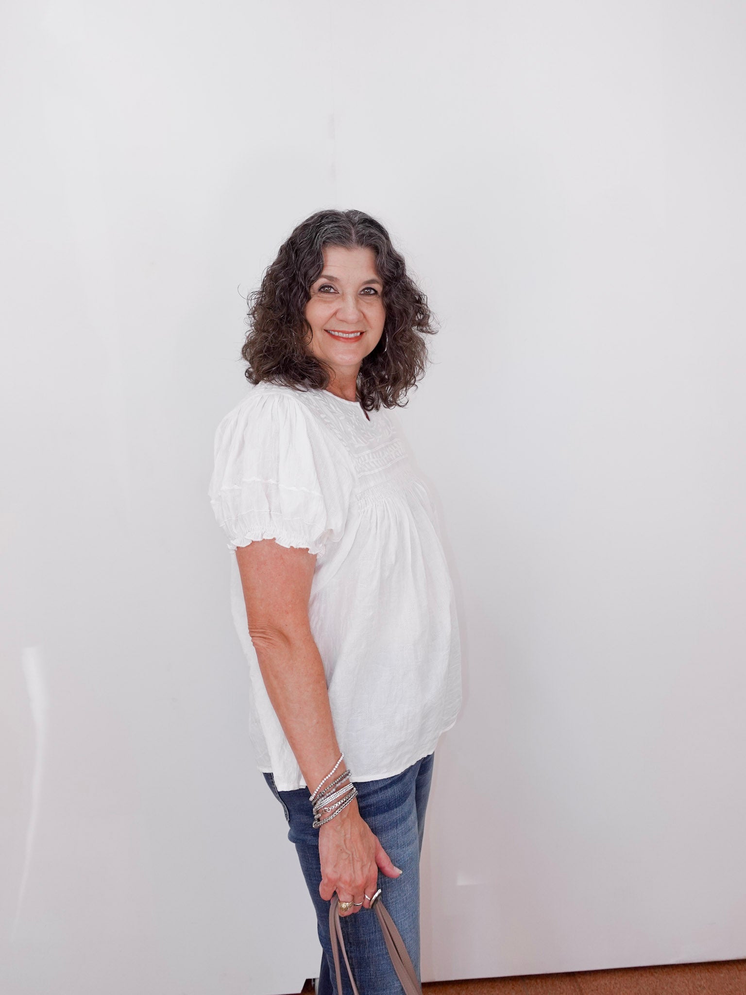Woman wearing a white blouse and blue jeans against a plain background