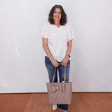 Woman holding a beige handbag against a white wall