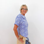Woman wearing a blue checkered shirt and beige pants, holding a blue handbag against a white background