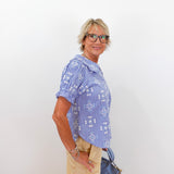 Woman wearing a blue checkered shirt and beige pants, holding a blue handbag against a white background