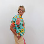 Person wearing a colorful floral shirt and beige pants against a white background