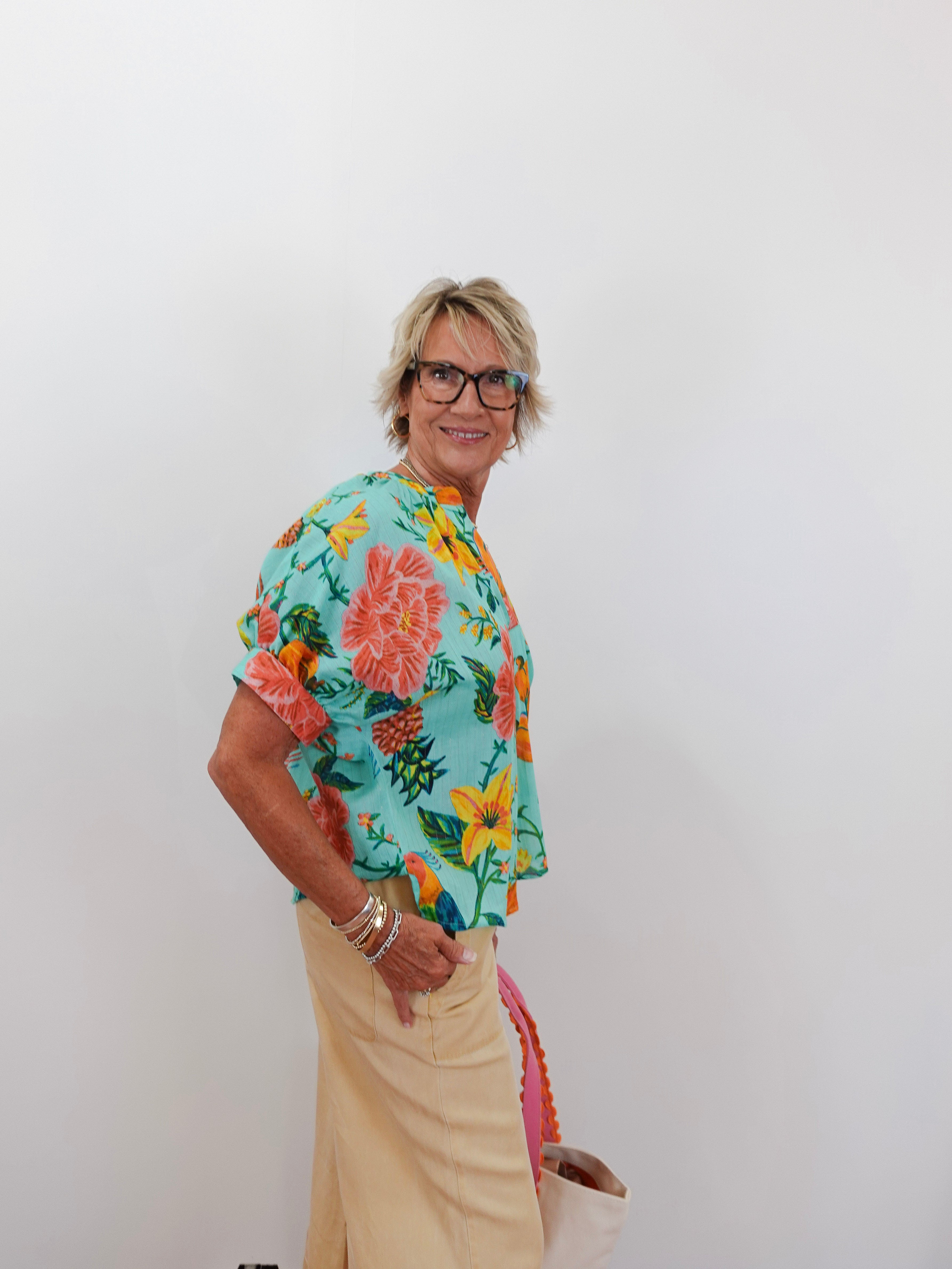 Person wearing a colorful floral shirt and beige pants against a white background