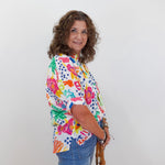 Woman wearing a colorful floral blouse and blue jeans against a white background