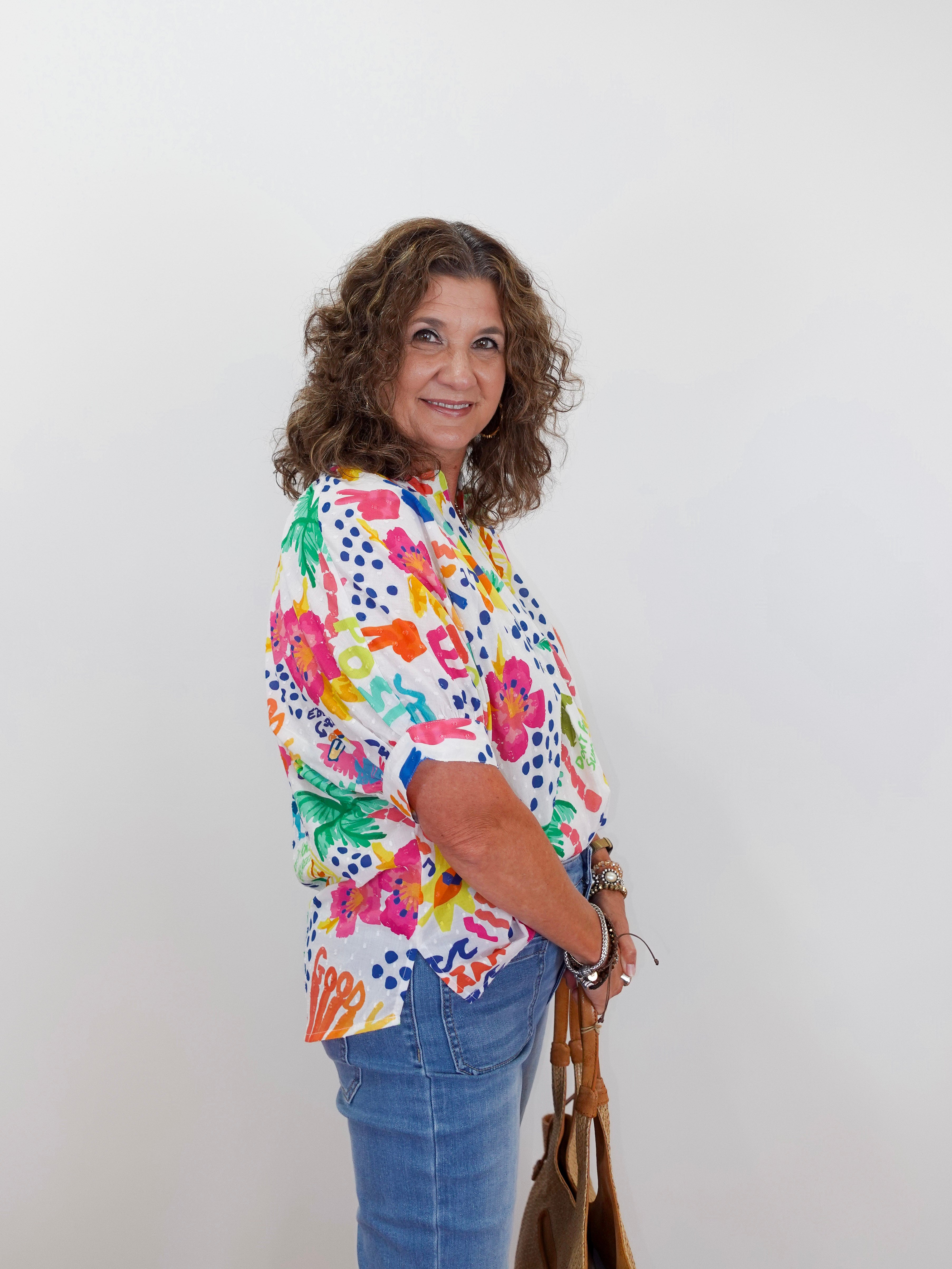 Woman wearing a colorful floral blouse and blue jeans against a white background