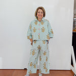 Woman wearing a light blue floral outfit standing against a white wall.