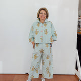 Woman wearing a light blue floral outfit standing against a white wall.