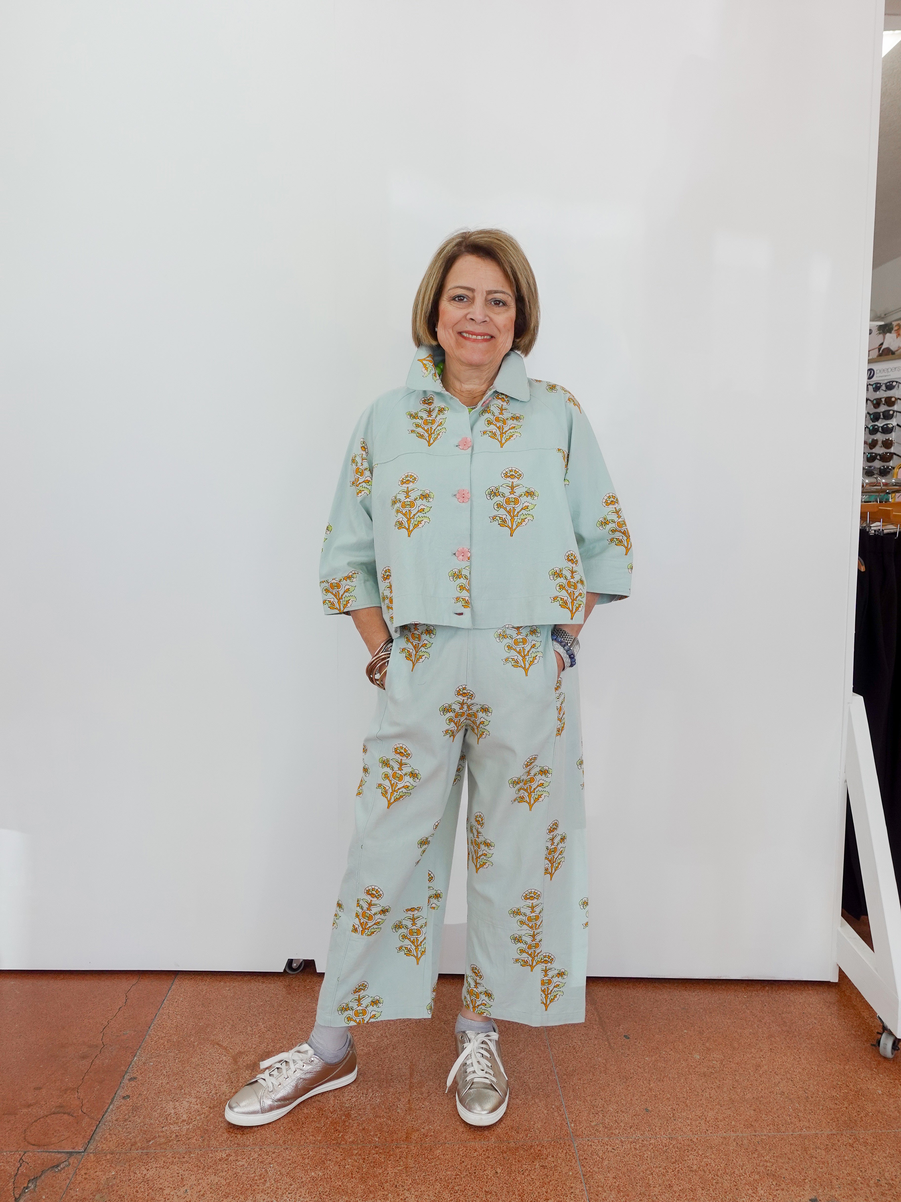 Woman wearing a light blue floral outfit standing against a white wall.