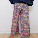 Person wearing floral-patterned pants and a denim jacket against a white wall.