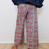 Person wearing floral-patterned pants and a denim jacket against a white wall.