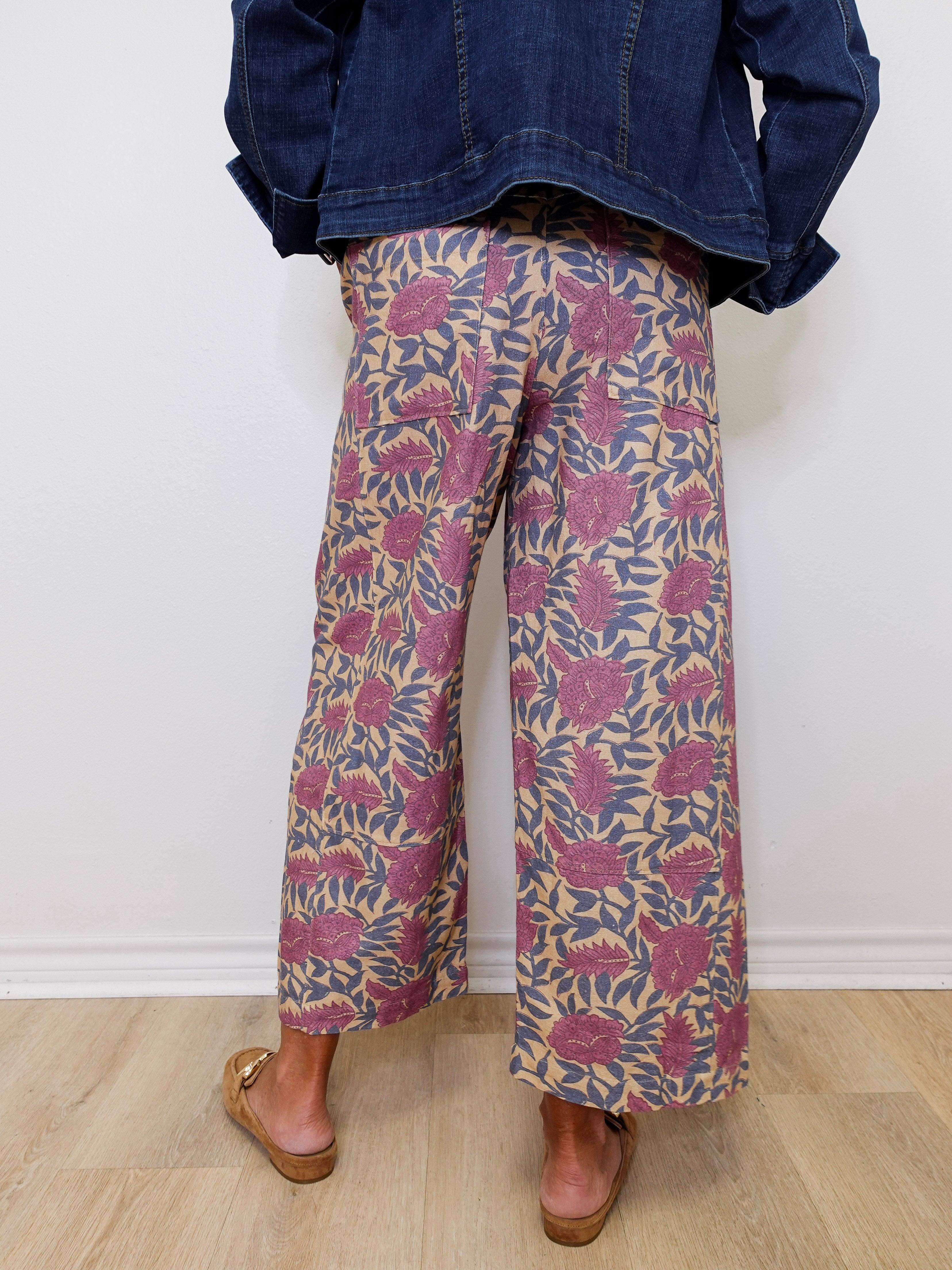 Person wearing floral-patterned pants and a denim jacket against a white wall.