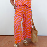 Person wearing a vibrant orange and pink zebra print outfit with a woven bag on a white background.