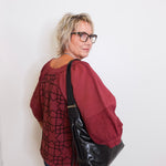 Person wearing a red patterned shirt and black leather bag against a white background