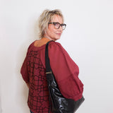 Person wearing a red patterned shirt and black leather bag against a white background