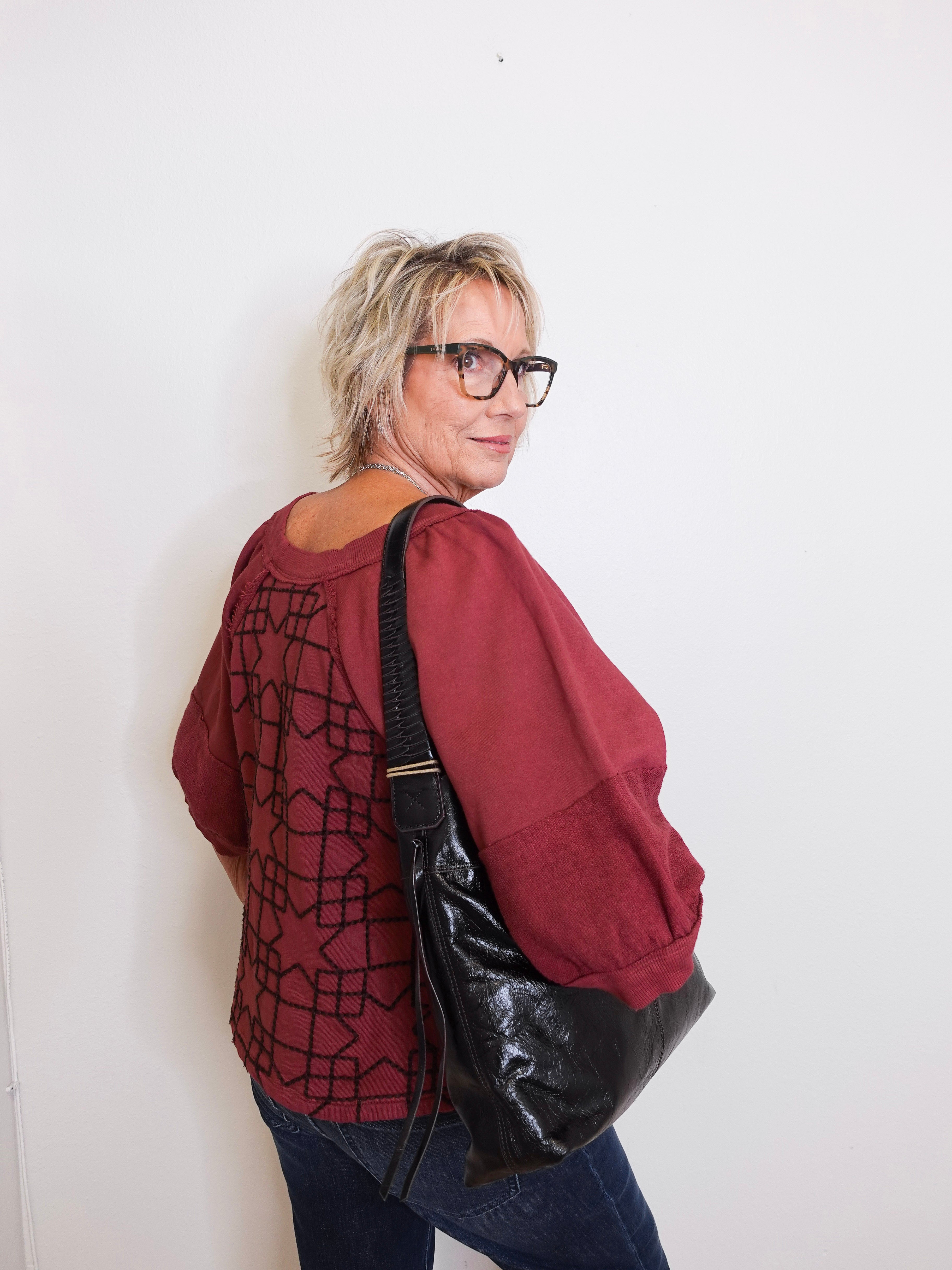 Person wearing a red patterned shirt and black leather bag against a white background