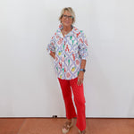 Person wearing a colorful patterned shirt and red pants against a white wall.
