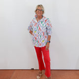 Person wearing a colorful patterned shirt and red pants against a white wall.