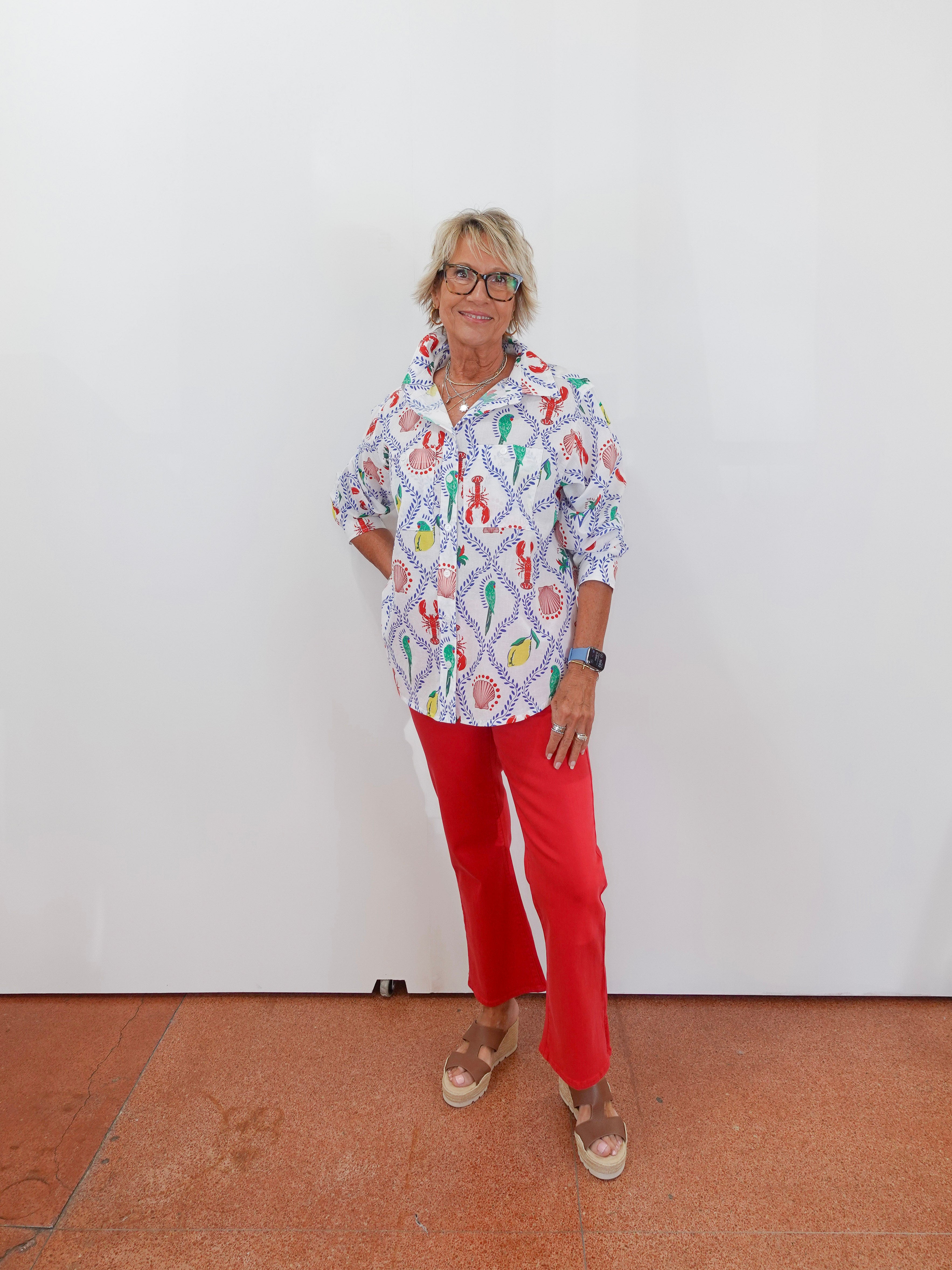 Person wearing a colorful patterned shirt and red pants against a white wall.