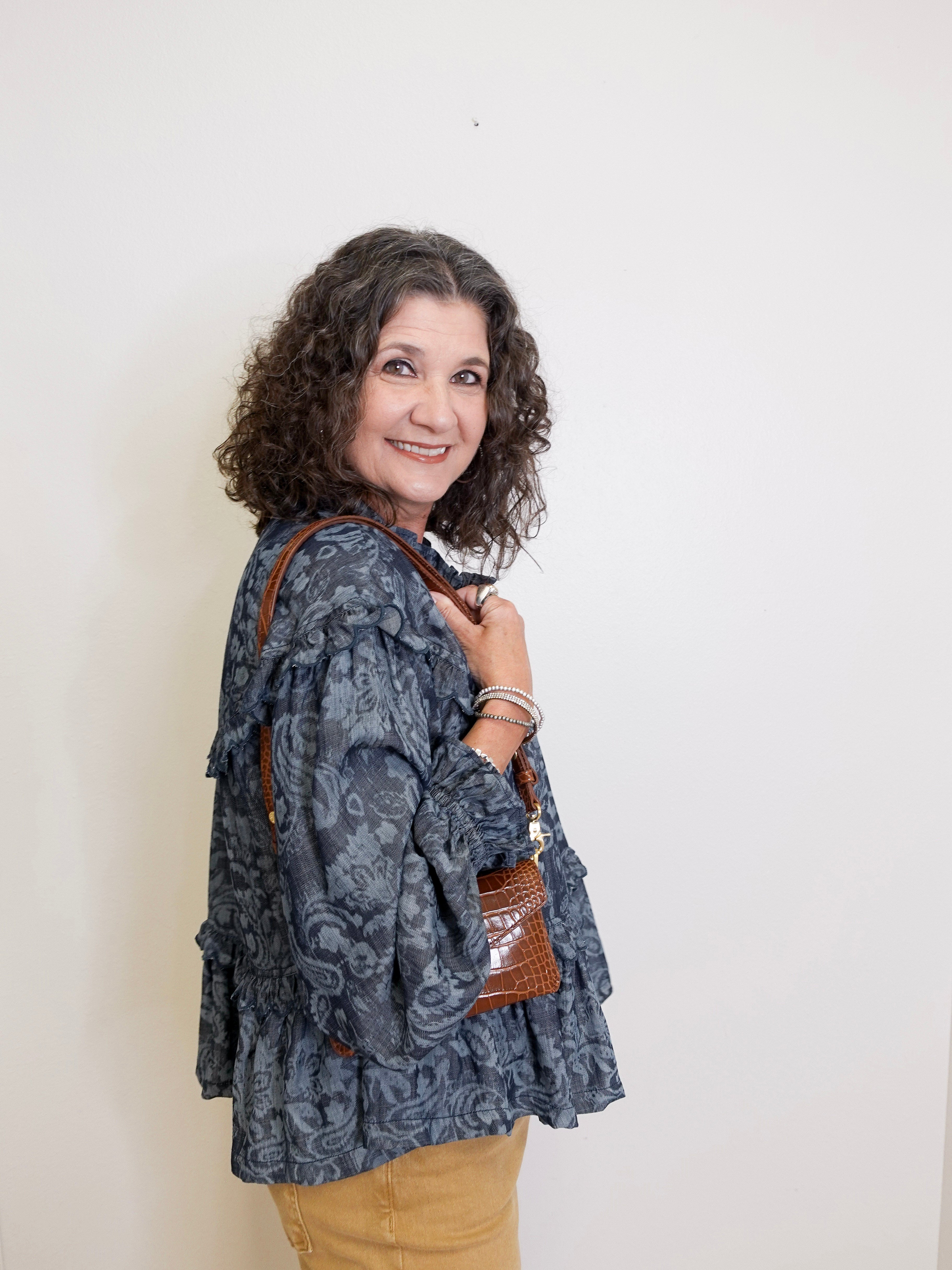 Woman wearing a patterned jacket and holding a brown bag against a white background