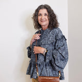 Woman wearing a patterned blouse and holding a brown handbag against a white background