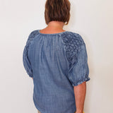 Person wearing a blue blouse with lace details on a plain background