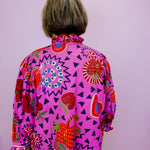 Person wearing a vibrant, patterned shirt with a pink background