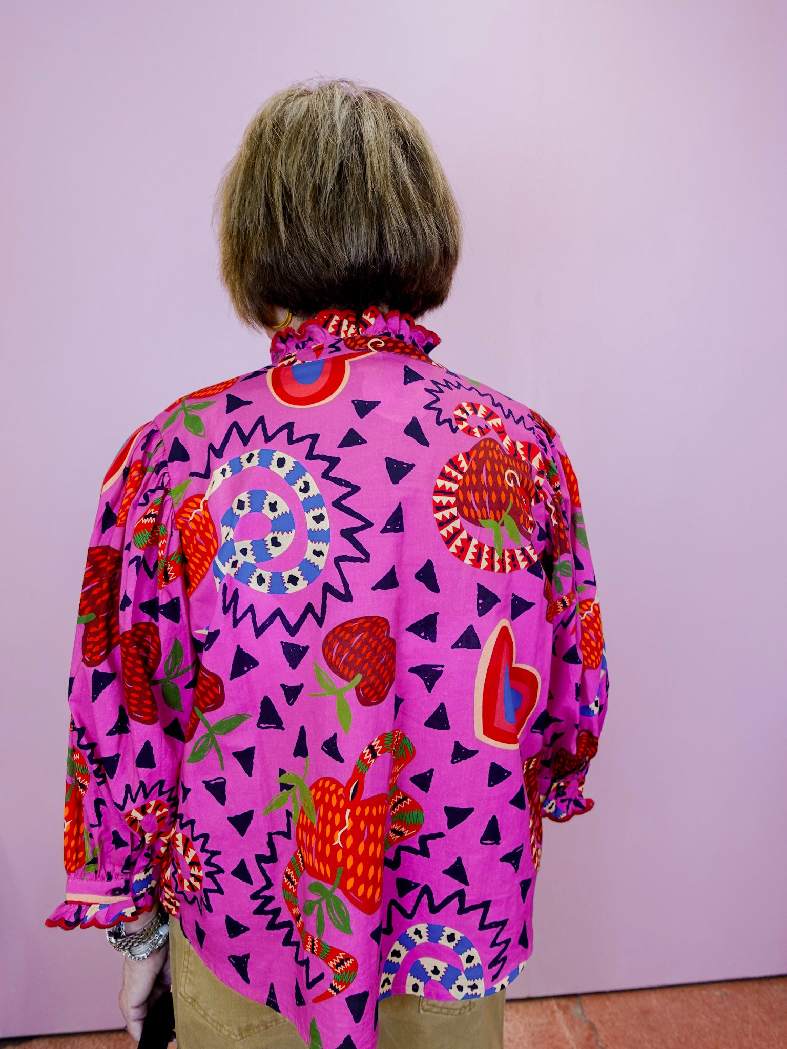 Person wearing a vibrant, patterned shirt with a pink background