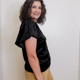 Woman wearing a black top and beige pants against a white background