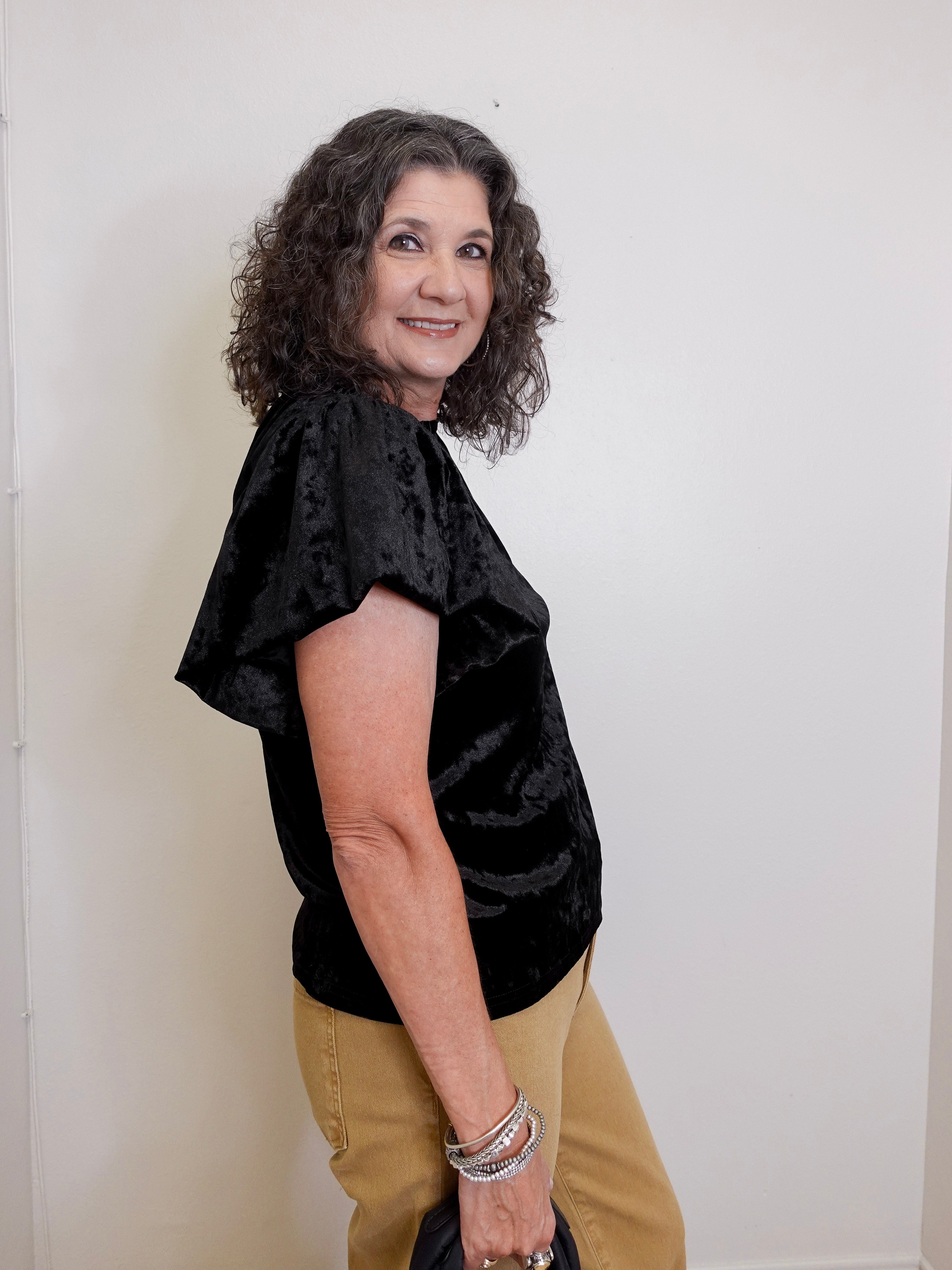 Woman wearing a black top and beige pants against a white background