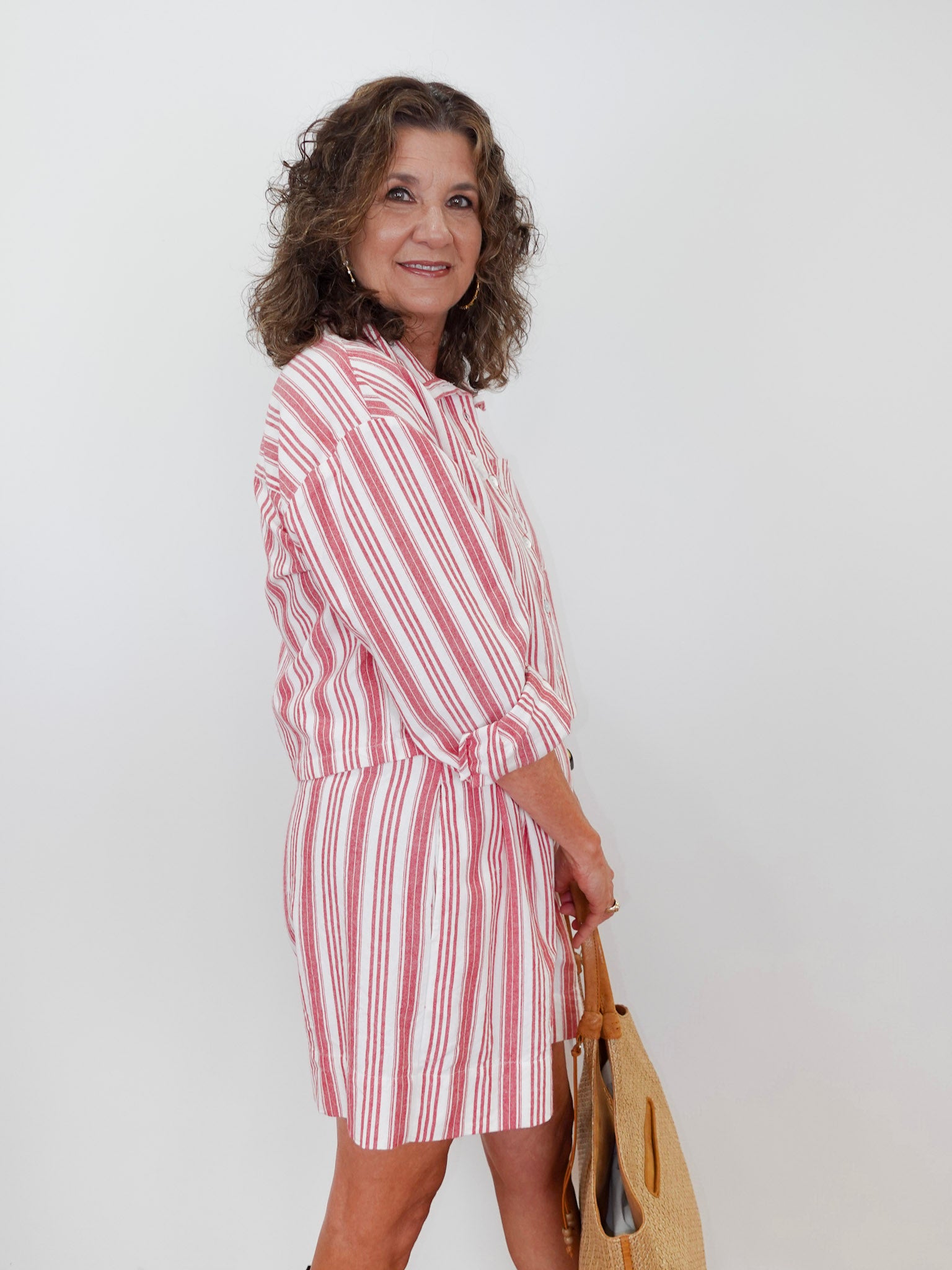 Woman wearing a red and white striped dress holding a beige bag against a white background