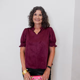 Woman wearing a burgundy blouse holding a colorful clutch against a plain background