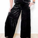 Person wearing black velvet wide-leg pants and a matching top against a white background