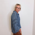 Person wearing a blue denim shirt and brown pants against a white wall