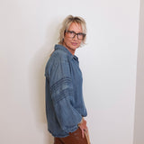 Person wearing a blue denim shirt and brown pants against a white wall