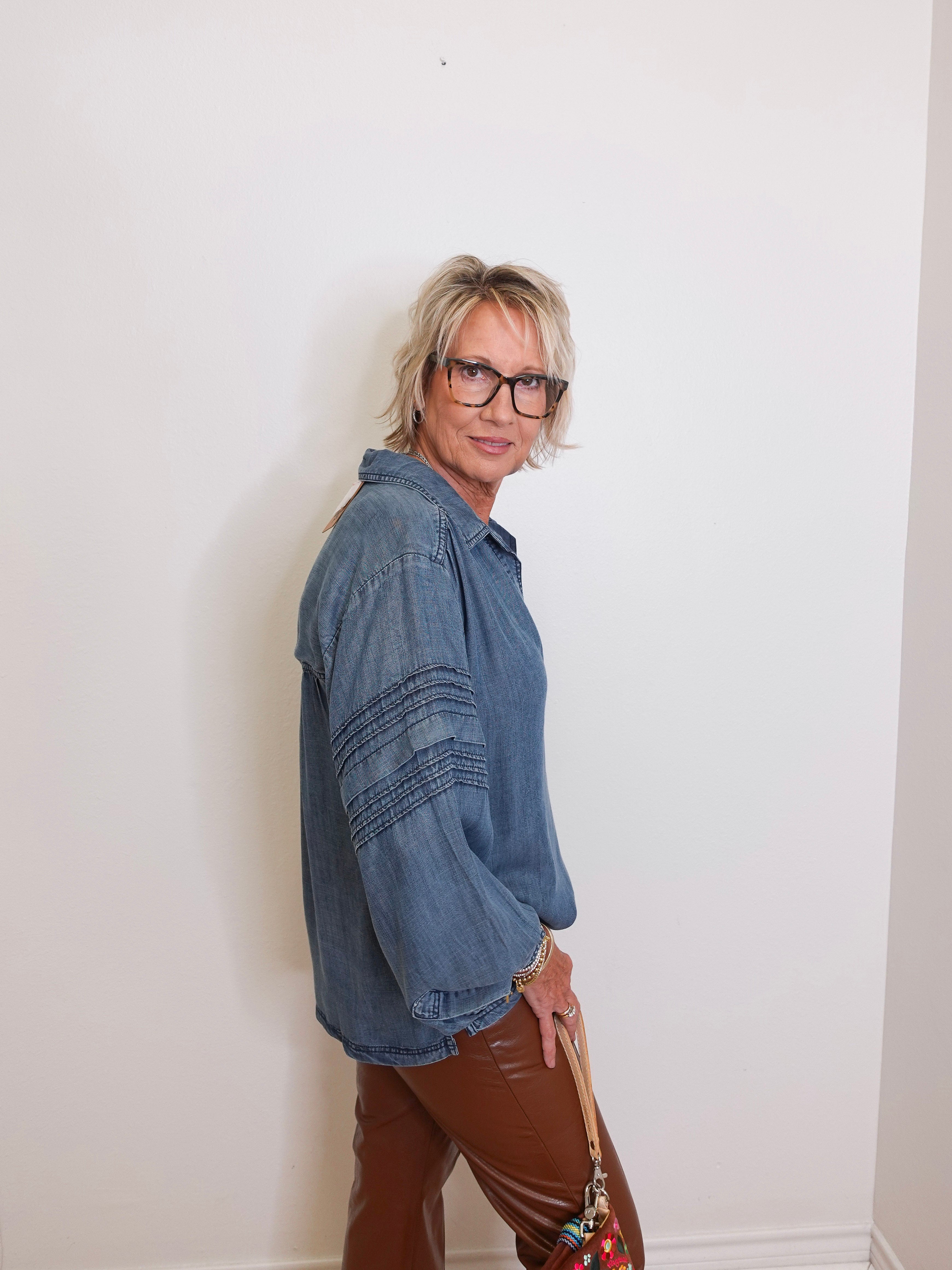 Person wearing a blue denim shirt and brown pants against a white wall