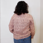 Person wearing a patterned shirt and jeans against a white wall