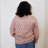Person wearing a patterned shirt and jeans against a white wall
