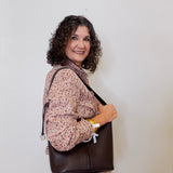 Woman holding a brown leather bag against a plain background