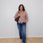 Woman wearing a patterned shirt and jeans standing against a white wall.