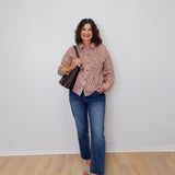 Woman wearing a patterned shirt and jeans standing against a white wall.