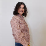 Woman wearing a patterned blouse and jeans against a plain background