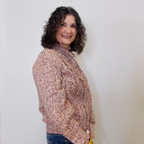 Woman wearing a patterned blouse and jeans against a plain background