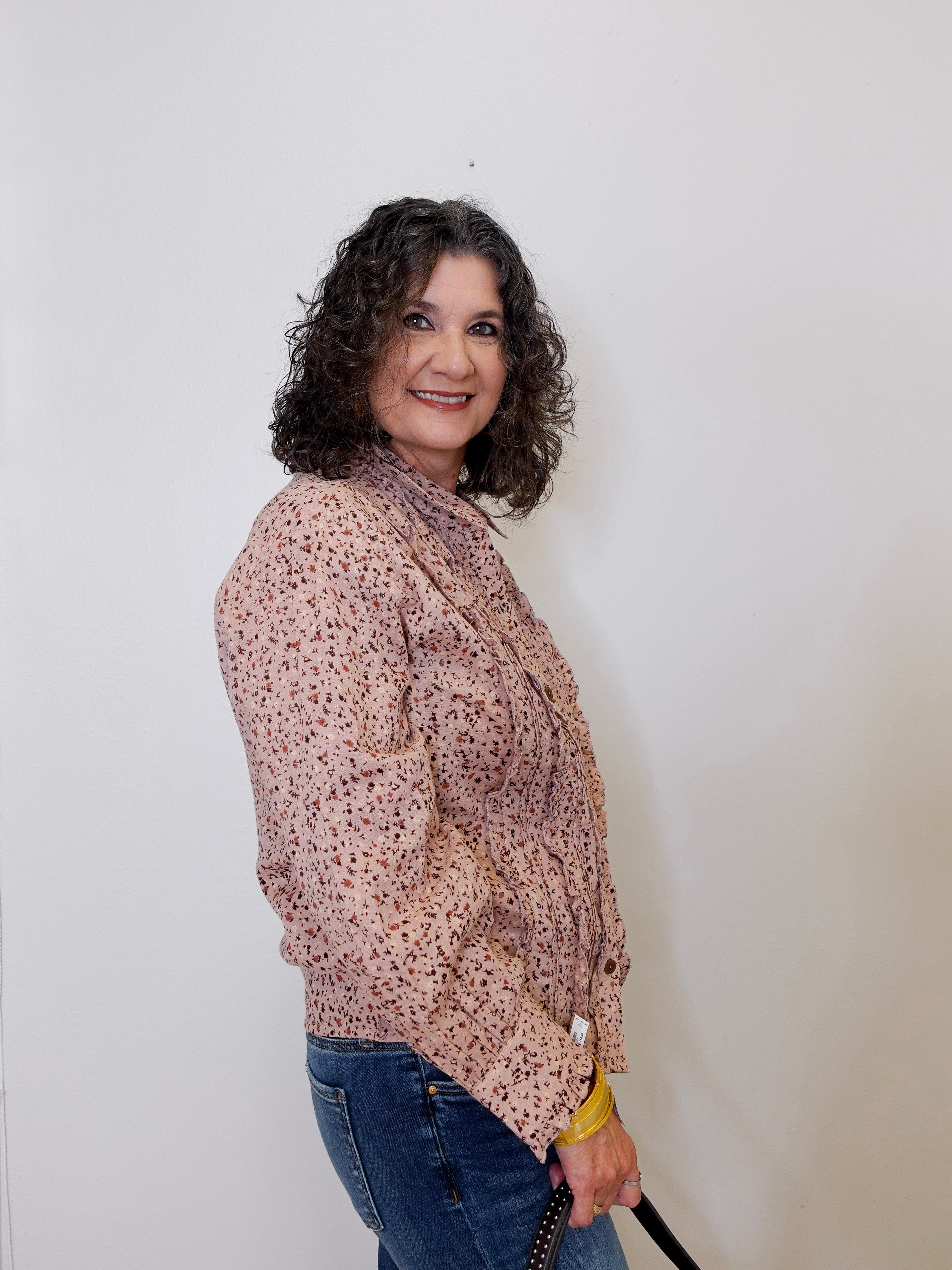 Woman wearing a patterned blouse and jeans against a plain background
