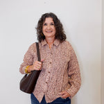 Woman wearing a patterned shirt and jeans, holding a brown bag against a white background
