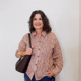 Woman wearing a patterned shirt and jeans, holding a brown bag against a white background
